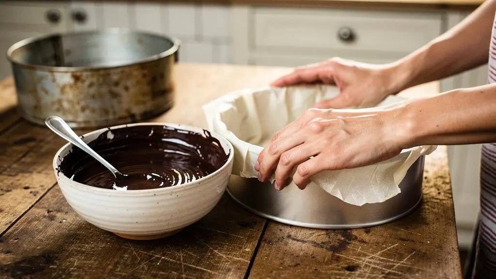 Mains chemisant un moule à moelleux au chocolat avec du papier sulfurisé dans une cuisine française, sans aucun pli visible